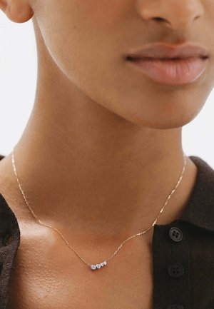 Primer plano de una persona que lleva un delicado collar de oro con cinco pequeños diamantes redondos graduados en una cadena fina.