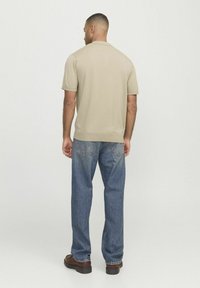Polo en tricot beige à manches courtes avec un ourlet droit, associé à un jean en denim bleu clair et des chaussures marron, vu de dos.