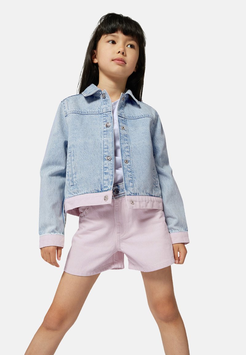 Lichtblauwe denimjas met een cropped ontwerp, knoopsluitingen, en roze shorts van zacht materiaal met zijzakken.