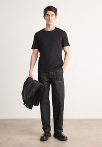 Černé tričko s krátkým rukávem, tmavě šedé džíny volného střihu, držící odpovídající denimovou bundu. Černé slip-on boty, minimalistický design.