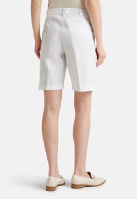 Pantaloni corti bianchi con orlo risvoltato e tasche posteriori, realizzati in tessuto liscio. Abbinati a mocassini chiari con tacco basso in legno.