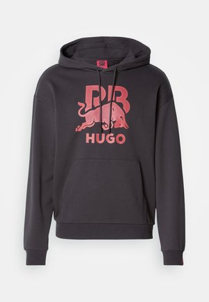 Hettegenser i mørkegrå bomull med en frontlomme. Har en stor rød Bull-logo og «HUGO»-tekst trykket på brystet.