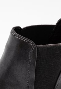 Černá kožená kotníková bota s elastickými bočními panely a kontrastním stehem. Hladká textura je doplněna strukturovaným tvarem.