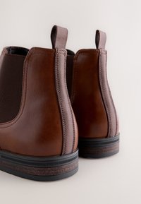 Brown leather ankle boots with elastic side panels and pull tabs. Features a textured brown rubber sole with a contrasting dark edge.
