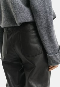 Schwarze Lederhosen mit zwei Gesäßtaschen, kombiniert mit einem grauen Strickpullover mit gerippten Bündchen und lockerer Passform, der eine matte Textur betont.