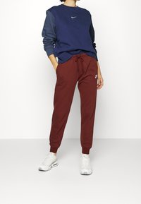 Marinblå och vinröd Nike sweatshirt och joggers. Sweatshirten har rund halsringning och logotyp; joggers har elastisk midja och muddar. Vita sneakers.