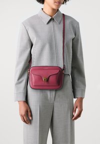 Borsa a tracolla in pelle magenta con chiusura dorata, caratterizzata da una superficie testurizzata, dotata di una tracolla regolabile e di un design minimalista.