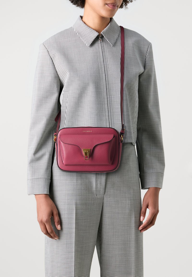 Borsa a tracolla in pelle magenta con chiusura dorata, caratterizzata da una superficie testurizzata, dotata di una tracolla regolabile e di un design minimalista.