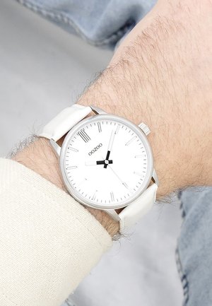 Montre OOZOO blanche avec un cadran rond minimaliste, un boîtier en argent et un bracelet en cuir blanc. Aiguilles des heures et des minutes noires, avec des repères simples.