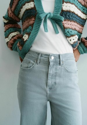 Persoană purtând blugi albaștri deschiși, cu talie înaltă, și un cardigan croșetat multicolor legat la piept peste un top alb.