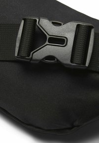 Sort stofpose med en stor plastikspænde med en struktureret overflade, forstærket webbing-strop og glatte, afrundede kanter.