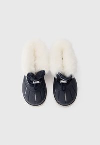 Botas de invierno negras de tamaño infantil con forro de piel sintética blanca y cierres de cordones ajustables, mostradas desde arriba sobre un fondo blanco.