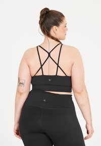 Zwarte sport-bh met een ontwerp met bandjes op de rug en platte naden; gecombineerd met hoge zwarte leggings van textuurstof.