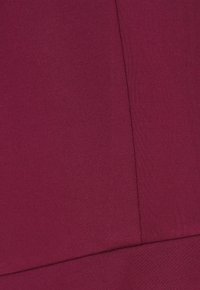 Zbliżenie na bordową tkaninę z widocznym szyciem i liniami szwów tworzącymi geometryczne panele.