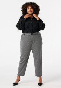 Zwarte overhemd met een subtiele print, gecombineerd met grijs geruite broek met een riem. Zwarte hoge hakken maken de look af.