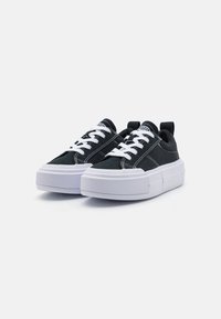 Svarte lerrets sneakers med hvite snører, en tykk hvit gummisåle, og en bakre trekker. Har kontrasterende sømdetaljer.