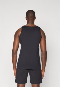 Svart bomullstopp med rund hals, med brede armåpninger og rett kant, iført mørke shorts. Glatt tekstur, minimalistisk design.