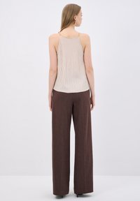 Beige geribde tanktop met gouden kettingbandjes, gecombineerd met bruine wijde broek, met een gestructureerde stof en een ontspannen silhouet.