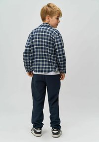 Camisa de cuadros en tonos navy con rayas blancas, combinada con pantalones jogger oscuros y zapatillas negras. La camisa tiene mangas largas y detalles de botones.