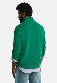 Grøn sweatshirt med høj krave, ribstrikkede manchetter og kant. Blød tekstur. Matchet med lyseblå skjorte med knapper og denimjeans.