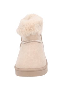 Beige mockasins ankelstövlar med en fluffig pälskant, mjuk textur, platt sula och dekorativ stickning längs kanterna.