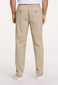 Beżowe spodnie wykonane z lekkiego materiału o luźnym kroju. Posiadają tylne kieszenie zapinane na guziki oraz elastyczny pas.