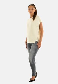 Maglione a maglia crema a maniche corte con zip laterali, abbinato a jeans grigi a vita media e svasati e scarpe nere con tacco alto.