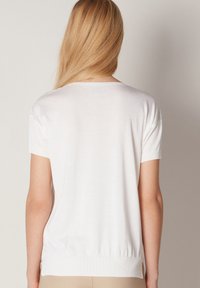 Biała krótka bluzka na krótki rękaw o gładkiej fakturze, z prążkowanym dekoltem i dołem, w luźnym kroju, z bocznymi rozcięciami na dole.