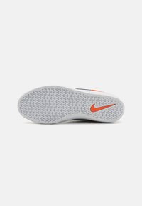 Solado de sapatilha Nike em borracha cinza, com padrão hexagonal, apresentando um proeminente swoosh vermelho da Nike na lateral.