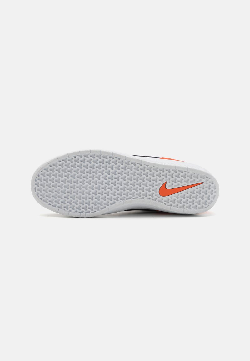 Semelle en caoutchouc gris de chaussure Nike, avec un motif hexagonal, arborant un célèbre swoosh Nike rouge sur le côté.