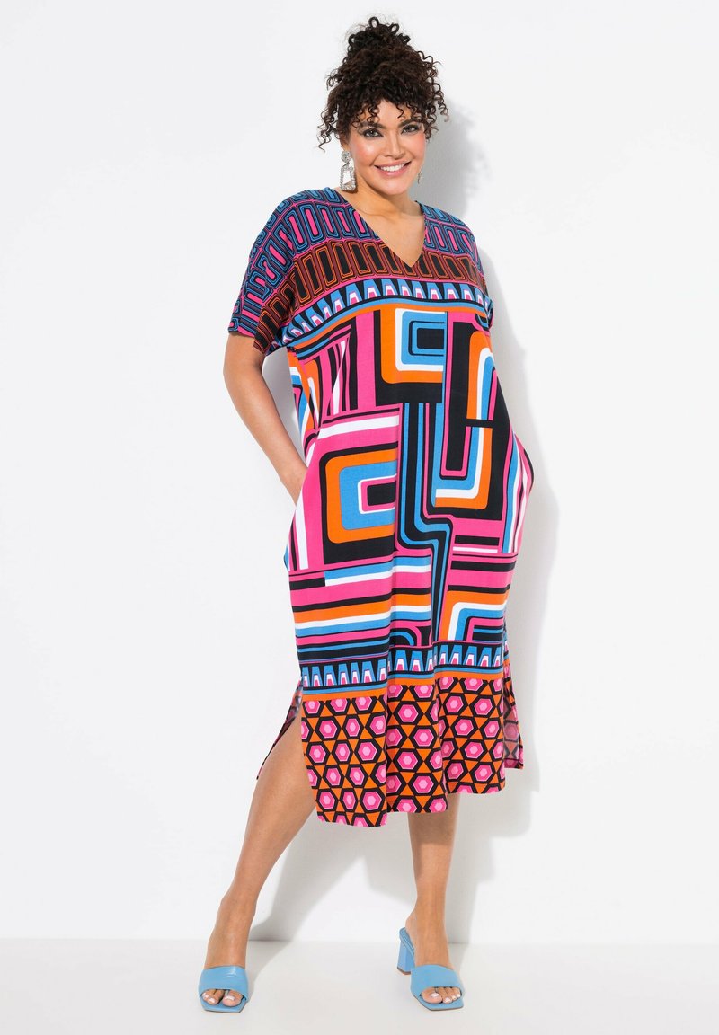 V-Ausschnitt-Kleid mit leuchtenden geometrischen Mustern in Pink, Schwarz, Orange und Blau. Kurze Ärmel, Seitenschlitze und ein Rüschensaum.