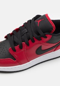 Baskets en cuir rouge et noir avec des lacets noirs, une boîte à orteils perforée et une semelle en caoutchouc blanche. Présente le logo emblématique sur la languette et le côté.