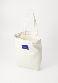 Canvas-Shopper in Off-White mit blauen Nähten und einem rechteckigen blauen Logo-Patch. Mit zwei stabilen Schulterträgern.
