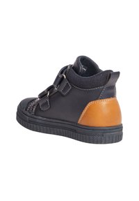 Zapatilla infantil tipo media en cuero negro, con detalles en marrón, puño elástico y correas laterales. Suela de goma texturizada y costuras decorativas.