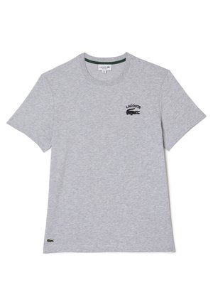 Jasnoszary T-shirt z krótkim rękawem, z czarnym logo Lacoste i tekstem po lewej stronie klatki piersiowej oraz małym zielonym logo krokodyla w pobliżu dolnego brzegu.
