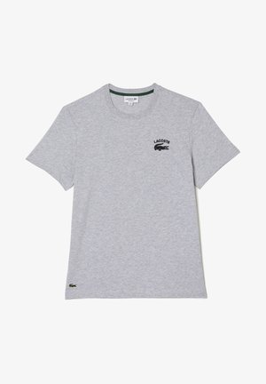 Jasnoszary T-shirt z krótkim rękawem, z czarnym logo Lacoste i tekstem po lewej stronie klatki piersiowej oraz małym zielonym logo krokodyla w pobliżu dolnego brzegu.