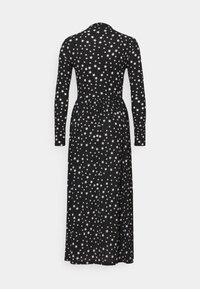 Svart maxiklänning med lång ärm, prydd med ett spritt mönster av vita stjärnor. Mjuk väv, figursydd midja och en flödande kjol.