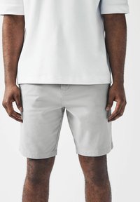 Pantalones cortos gris claro fabricados con una mezcla de algodón, que presentan bolsillos laterales, un diseño frontal simple y un dobladillo recto.