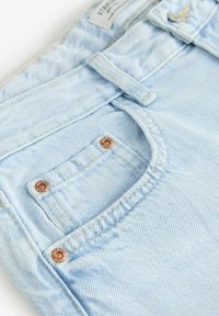 Gaiši zili denim džinsi ar nedaudz izbalējušu tekstūru, ar mazu kabatu un vara detaļām pie jostas.