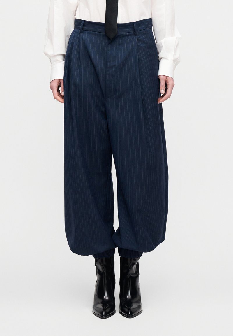 Φαρδιά παντελόνια σε ναυτικό μπλε  με κάθετες ρίγες και ψηλή μέση, με πιέτες στο μπροστινό μέρος και λεία υφή, συνδυασμένα με γυαλιστερά μαύρα μποτάκια αστραγάλου.