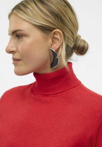 Grandi orecchini argentati a forma di mezzaluna con una finitura lucida. Il modello indossa un maglione rosso a collo alto.