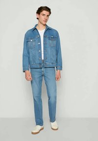 Jachetă din denim de culoare albastru deschis, cu două buzunare pe piept, închidere cu butoane și guler, asortată cu blugi de culoare albastru deschis și adidași albi.