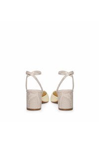 Sandalias de tacón beige con un upper texturizado que presenta un patrón geométrico, correas cruzadas en el tobillo y un diseño de punta redondeada y suave.