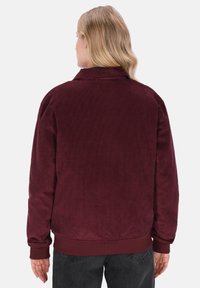 Giacca in corduroy bordeaux con una texture morbida, polsini e colletto a costine. Presenta una vestibilità morbida e un design minimalista sul retro.