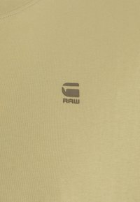 Svetle žluté tričko s kulatým výstřihem a jemnou texturou. Na přední straně se nachází malé černé logo "RAW" pro branding.