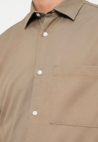 Camasa cu nasturi, din țesătură khaki, având guler ascuțit, buzunar frontal și închidere cu un singur nasture. Textură netedă, mată.