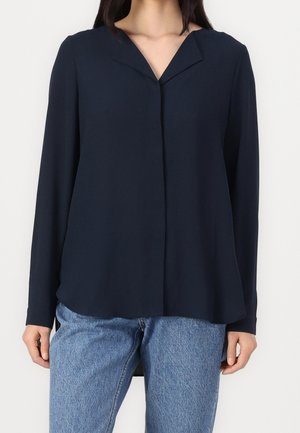 Blusa a maniche lunghe blu navy con scollo a V, tessuto morbido, chiusura frontale con bottoni e vestibilità comoda, abbinata a jeans in denim azzurro chiaro.