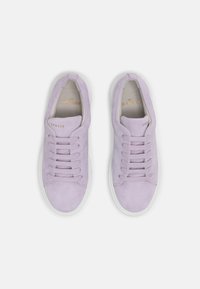 Lila mockaskor med rund tå, sex öglor med snören och en vit gummisula. Guld-logotyp inuti skon.