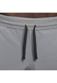 Pantalones cortos deportivos grises con una tela ribeteada texturizada, una cinturilla elástica y cordones negros para un ajuste ajustable.
