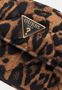 Portafoglio trapuntato con motivo a stampa leopardata nelle tonalità di marrone e nero. Presenta un accento dorato a forma di triangolo con il logo Guess.